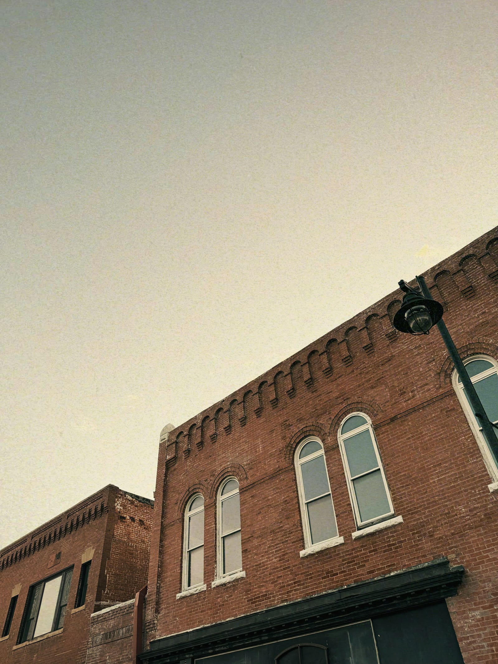 A red-brick building with arched upper windows and a corbeled cornice on a small-town street.