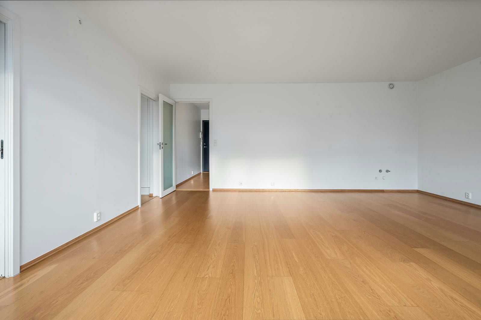 An empty room with warm hardwood floors and bright white walls.